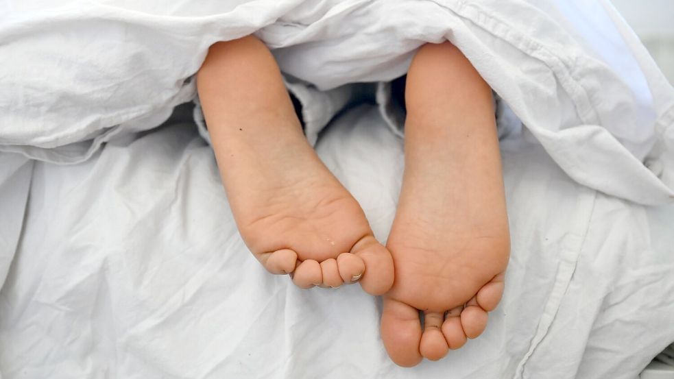 Die nackten Füße und Pyjamahose einer Frau sind unter einer Bettdecke zu sehen. Foto: Elisa Schu/dpa