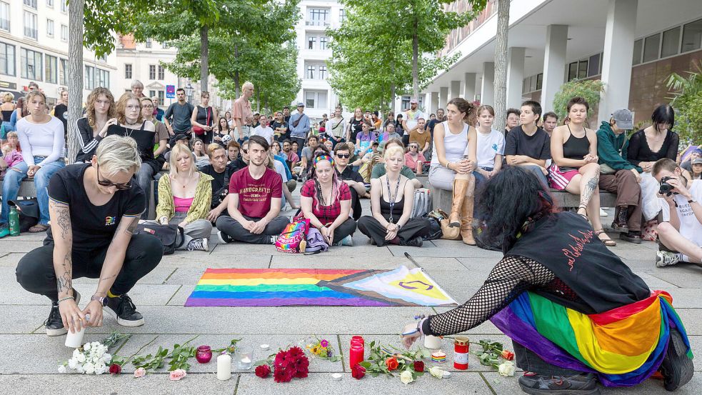 Blumen und brennende Kerzen werden bei der Mahnwache zum Anschlag auf den CSD in Berlin von Queer Pride Dresden und weiterer Gruppen auf den Boden vor einer Regenbogenfahne gelegt. Foto: DPA