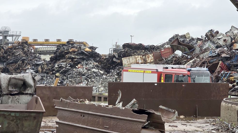 Am Freitagvormittag räumten Mitglieder der Feuerwehr die Einsatzstelle am Leeraner Hafen auf. Im Hintergrund ist der vom Brand betroffene Abfallhaufen gut zu erkennen. Foto: Bodo Wolters
