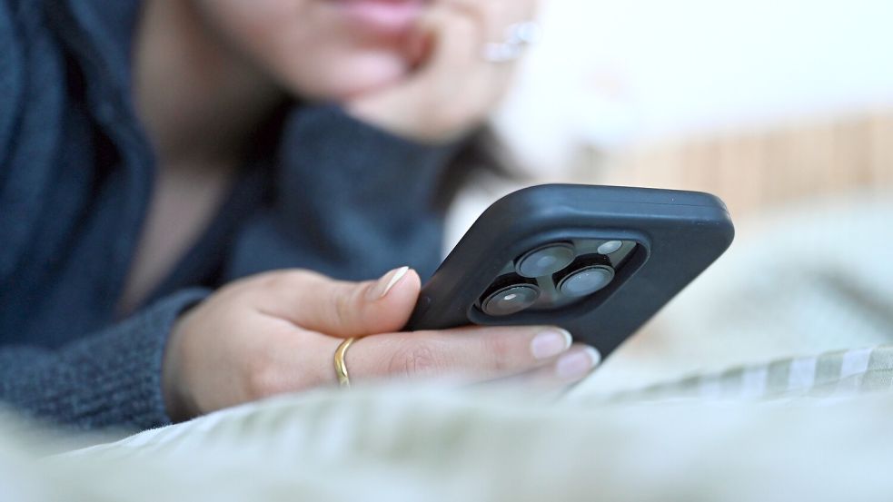Eine junge Frau liegt mit dem Smartphone in der Hand auf dem Bett. Foto: Elisa Schu/dpa