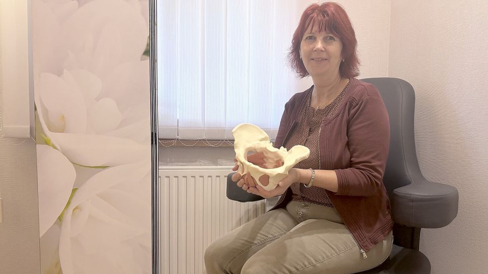 Elke Trauernicht sitzt in ihrer Praxis auf einem der Beckenbodenstühle und zeigt ein Modell, anhanddessen zu sehen ist, wo der Beckenboden sitzt. Foto: Christin Wetzel